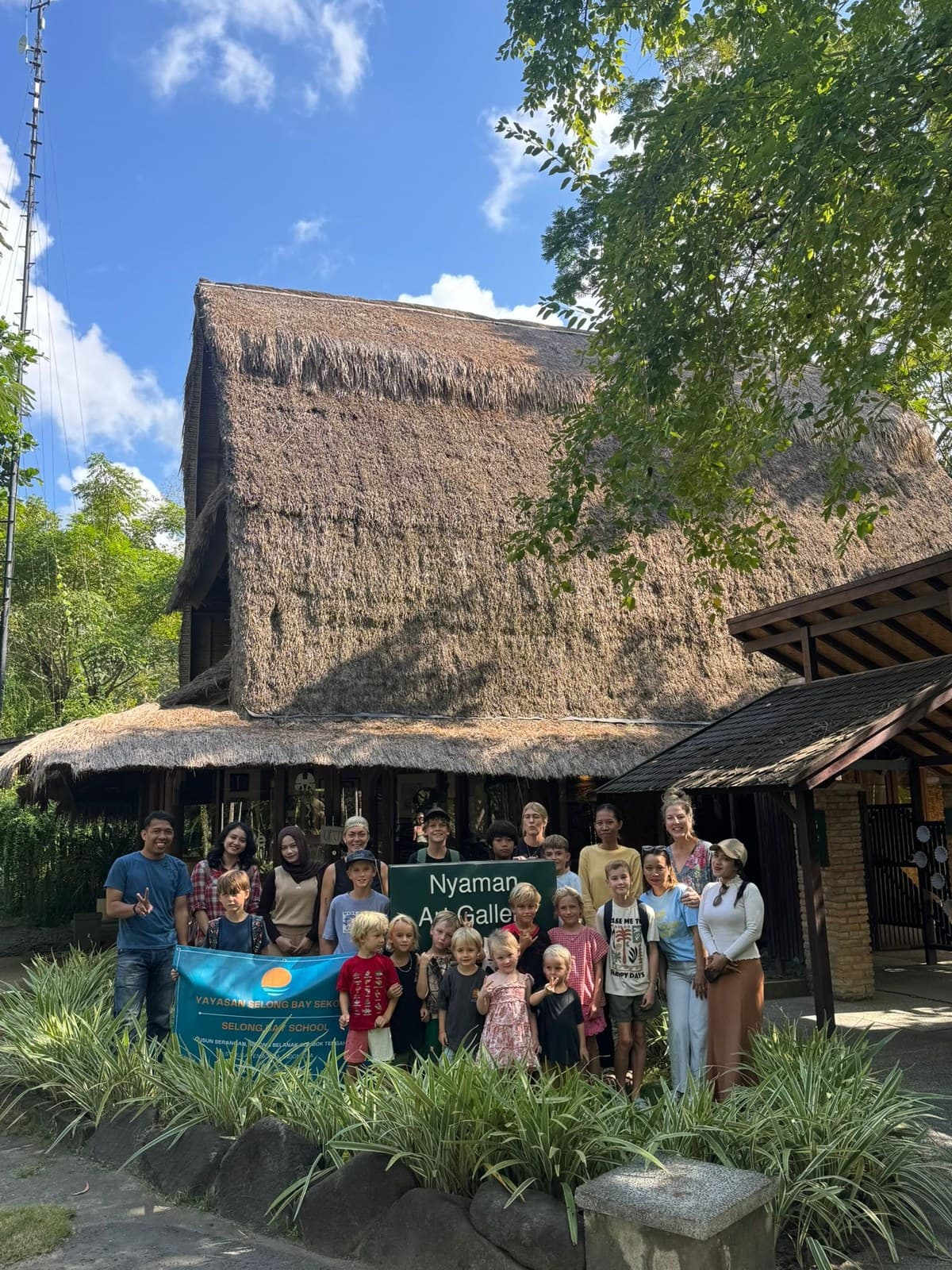 Selong Bay School students and staff on a community outing to Nyaman Art Gallery, holding a Yayasan Selong Bay Sekolah banner