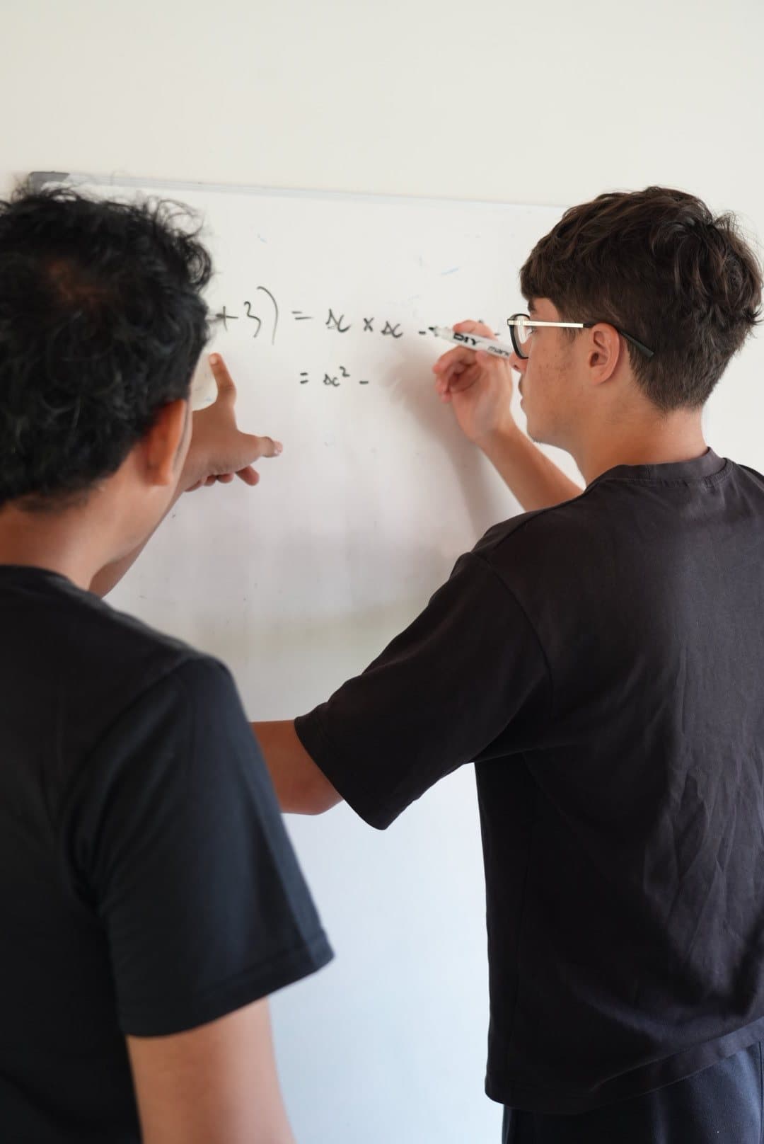 A secondary school student solving algebra at the whiteboard with a teacher